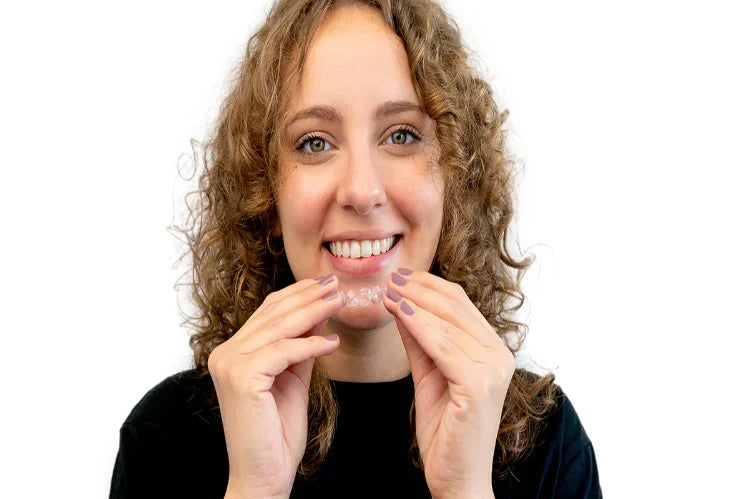 A woman smiling and putting on a dental retainer