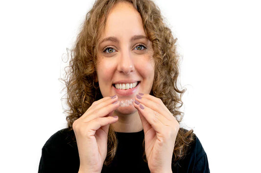 A woman smiling and putting on a dental retainer