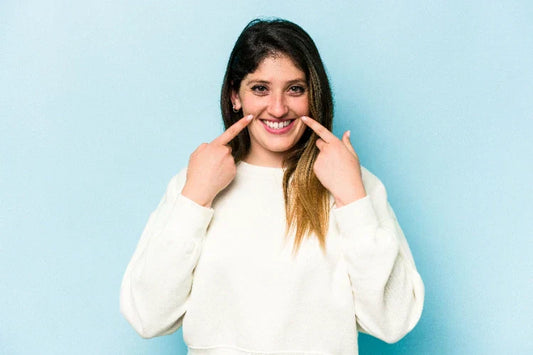 An image of a woman smiling while pointing fingers at her smile