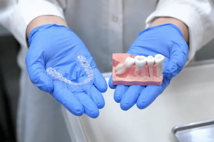  A dentist holding an aligner tray in one hand and a denture model showing an erupting wisdom tooth in the other.
