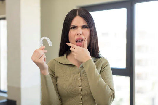 An image of a girl holding aligners with her mouth and eyes wide open and her hand on her chin.