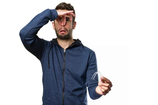  A guy holding a smelly retainer in one hand and his nose with the other, indicating a bad smell.